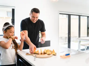Dad and daugher eating watermelon at the kitchen bench