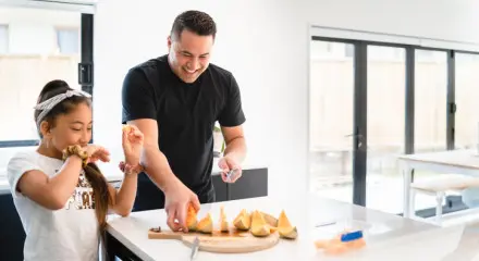 Dad and daugher eating watermelon at the kitchen bench