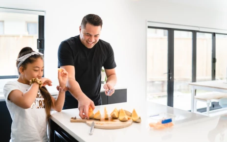 Dad and daugher eating watermelon at the kitchen bench
