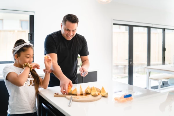 Dad and daugher eating watermelon at the kitchen bench