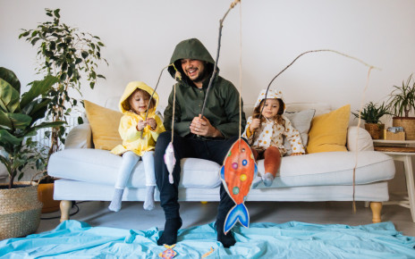 Young man and two kids dressed up in wet weather gear, sitting on the couch fishing for paper fish