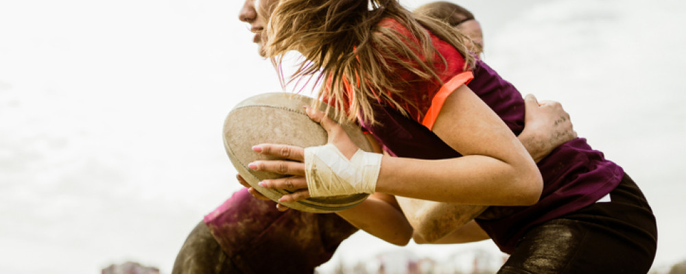 Girl running holding a rugby ball about to be tackled