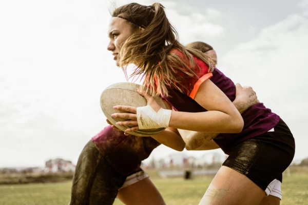 Girl running holding a rugby ball about to be tackled