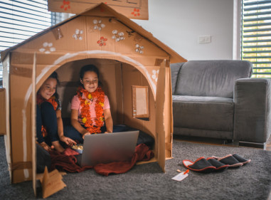 Two girls happily sitting in their cardboard house in the living room