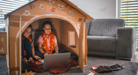 Two girls happily sitting in their cardboard house in the living room