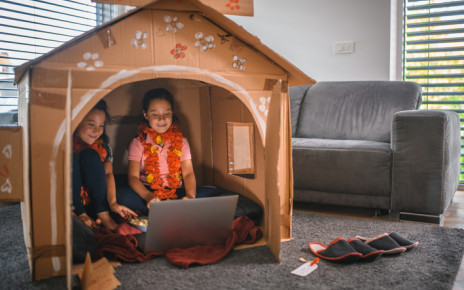 Two girls happily sitting in their cardboard house in the living room