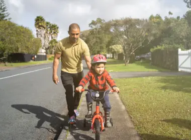 Dad holding on to the back of his son's bike as he learns to ride