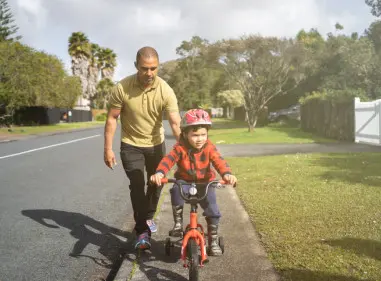 Dad holding on to the back of his son's bike as he learns to ride