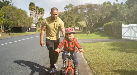 Dad holding on to the back of his son's bike as he learns to ride