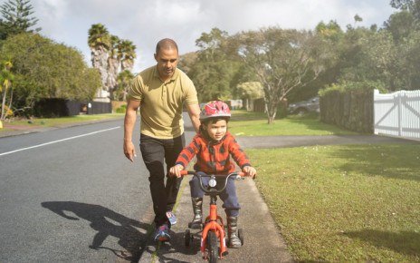 Dad holding on to the back of his son's bike as he learns to ride