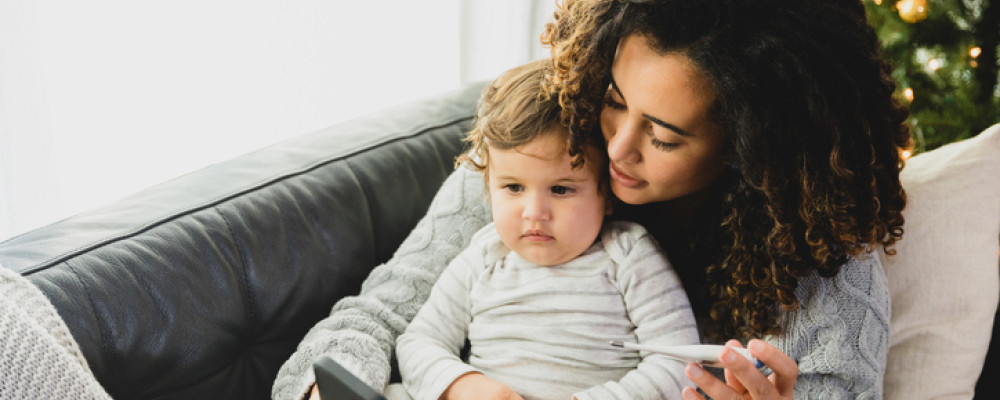 Mum checking toddler's temperature while cuddling on the couch