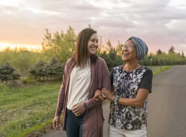 Two woman with arms linked smiling and walking at dusk