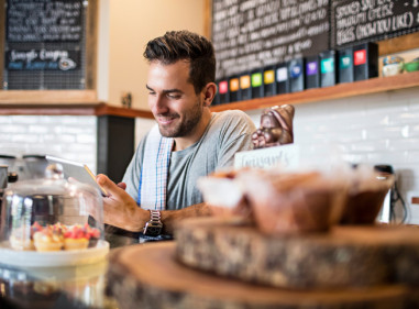 Man behind the counter in a cafe looking at his phone and smiling