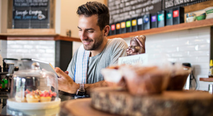 Man behind the counter in a cafe looking at his phone and smiling