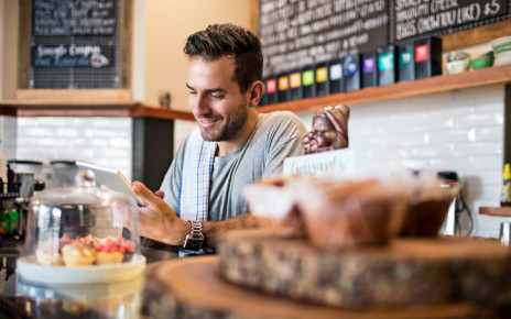 Man behind the counter in a cafe looking at his phone and smiling