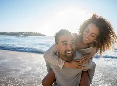 Smiling young man piggy-backing smiling partner in shallow waves at the beach