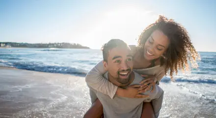 Smiling young man piggy-backing smiling partner in shallow waves at the beach