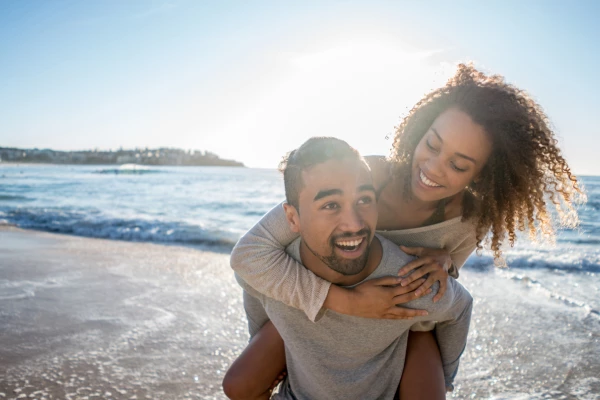 Smiling young man piggy-backing smiling partner in shallow waves at the beach