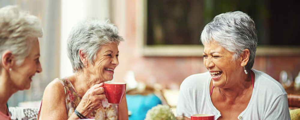 Three grey-haired women laughing and drinking tea