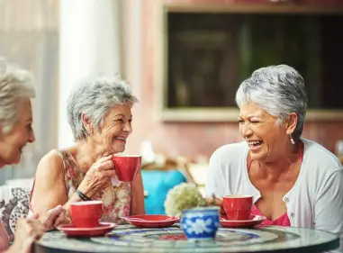 Three grey-haired women laughing and drinking tea