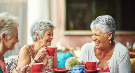 Three grey-haired women laughing and drinking tea