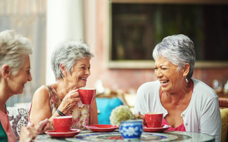 Three grey-haired women laughing and drinking tea