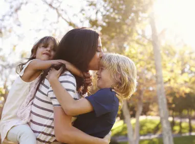 Woman cherishes moment with young children hugging her from the front and back