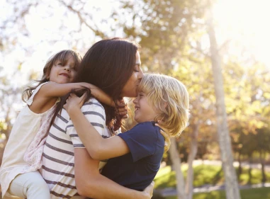 Woman cherishes moment with young children hugging her from the front and back