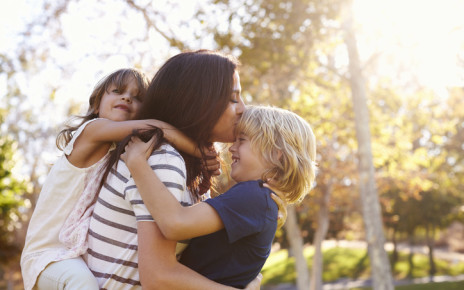 Woman cherishes moment with young children hugging her from the front and back