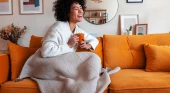 Woman sitting on couch with a blanket and holding a mug laughing