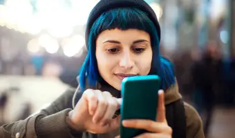 Person is holding up their mobile phone looking at it and pointing at the screen