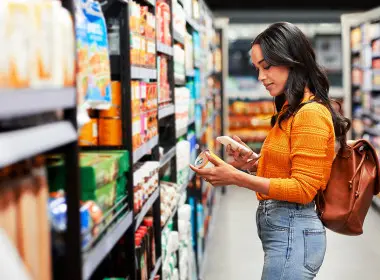 Person is holding a can of food in the supermarket aisle and looking at the ingredient list.