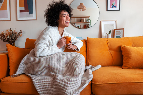 Woman sitting on couch with a blanket and holding a mug laughing