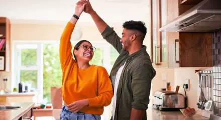 Couple are dancing in the kitchen and looking at each other laughing