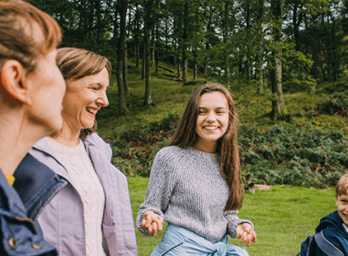 Family of four smiling and laughing together outdoors in a green forest setting.