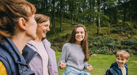 Family of four smiling and laughing together outdoors in a green forest setting.