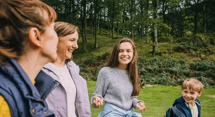 Family of four smiling and laughing together outdoors in a green forest setting.