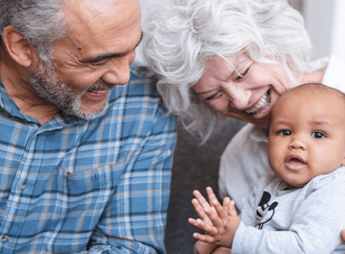Two older adults smiling and laughing with a young baby.