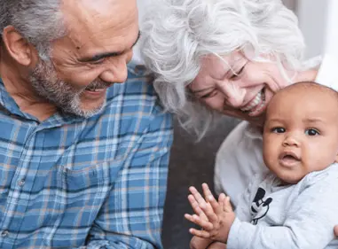 Two older adults smiling and laughing with a young baby.