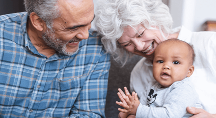 Two older adults smiling and laughing with a young baby.