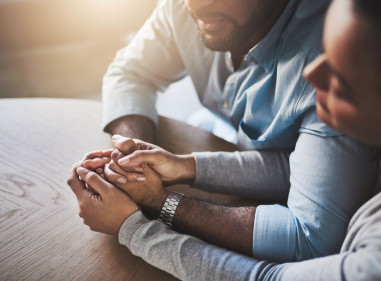 Close-up of two people's hands clasped together in support, sitting side by side.