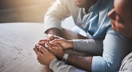 Close-up of two people's hands clasped together in support, sitting side by side.