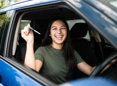 Young woman sitting in a car, smiling and holding up car keys.