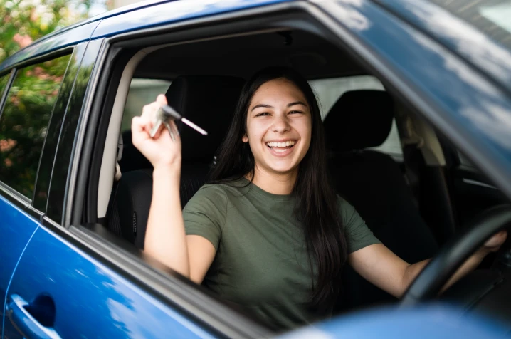 Young woman sitting in a car, smiling and holding up car keys.