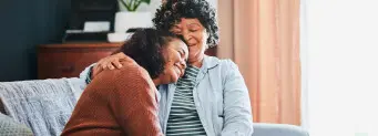 Two women in two generations smiling and hugging sitting in a couch giving a comfort feeling.