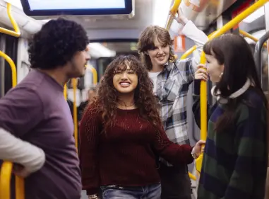 Four people standing and talking inside a public train, holding onto yellow handrails.