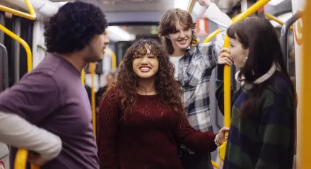 Four people standing and talking inside a public train, holding onto yellow handrails.