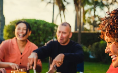 A group of people are eating a meal together at a table outside looking happy
