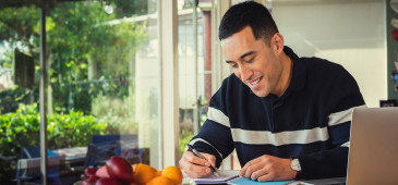 A man is sitting at the dining table with a notepad and pen