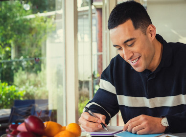 A man is sitting at the dining table with a notepad and pen